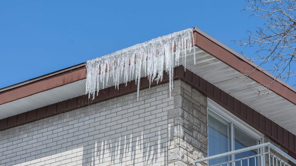 Stalactites de glace suspendues à l'avant-toit d'une maison en brique sous un ciel d'hiver