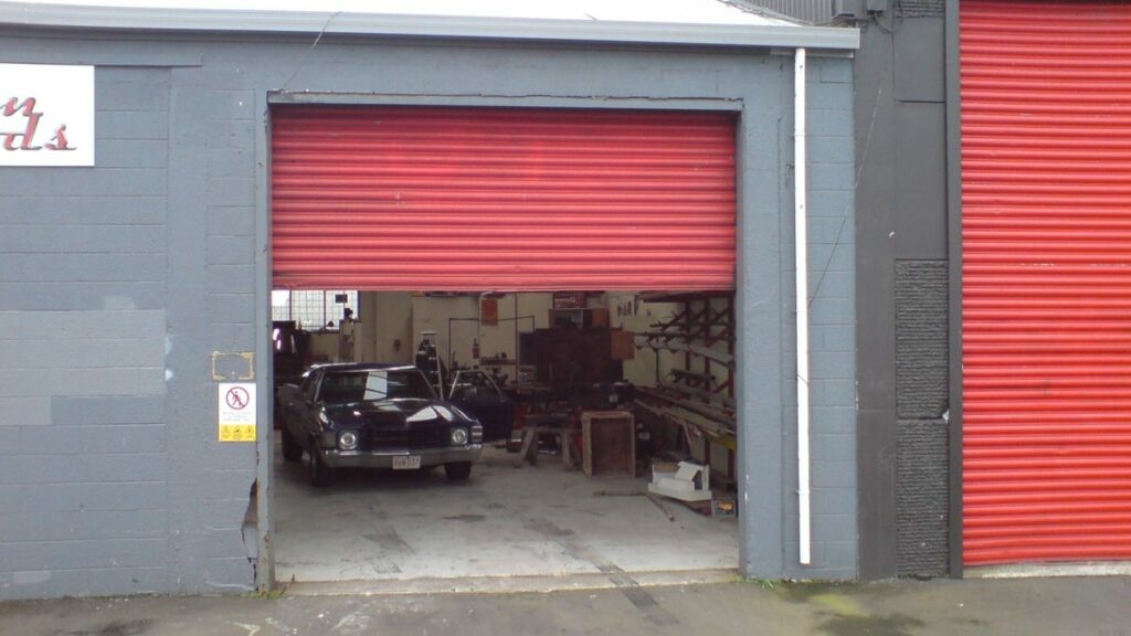 Garage équipé de deux rideaux métalliques rouges, dont un ouvert sur un atelier